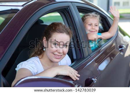 Mother with small daughter sitting in own car and waving at camera