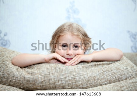 Small Caucasian child sitting on sofa with hands clasped on pillows
