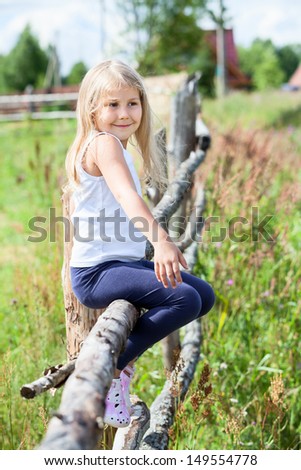 Beautiful Caucasian girl with blond hair sitting on a log in summer field