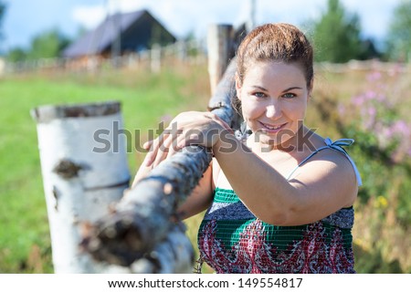 Attractive village woman in sundress posing near fence