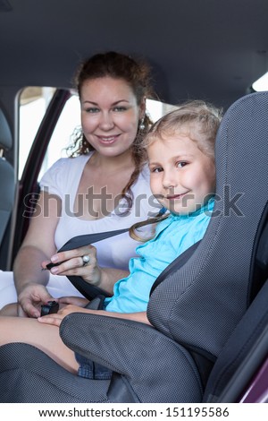 Safety children transportation with car seat in vehicle. Mother fastening daughter