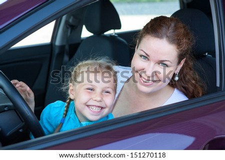 Happy toothy smiling mother with small daughter on driver seat inside of car