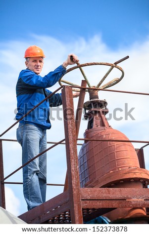 Mature manual worker turning huge valve gate at factory