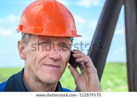 Senior manual worker in orange hardhat calling on the phone
