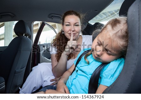 Mother with shh gesture when daughter asleep in car safety seat