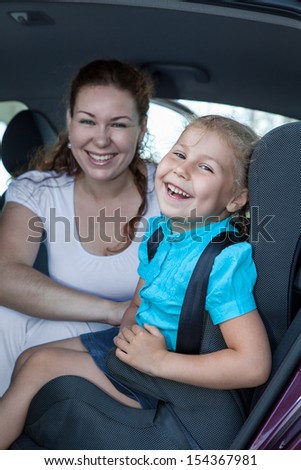 Cheerful Caucasian mother with daughter sitting in car safety seat