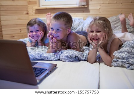 Children looking at laptop with cartoons showing before sleeping in bed