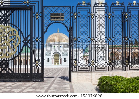 The entrance is through the lattice in the territory of the mausoleum with a sign schedule, Monastir, Tunisia.