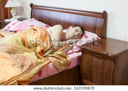 Sleeping Caucasian man in the bed. Early morning. Watch on the table