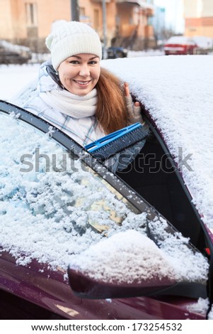 Smiling woman with snow brush and snowy car