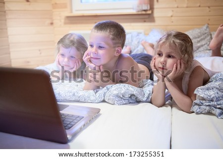 Three small children looking at laptop screen in bed