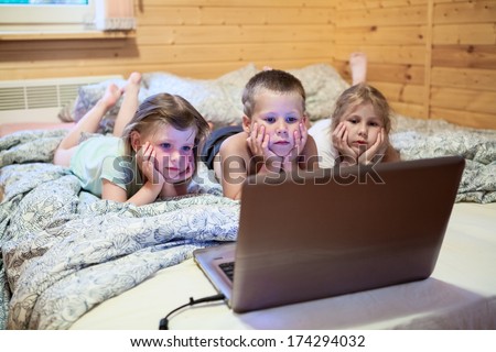 Three children looking at laptop monitor before sleeping in bed