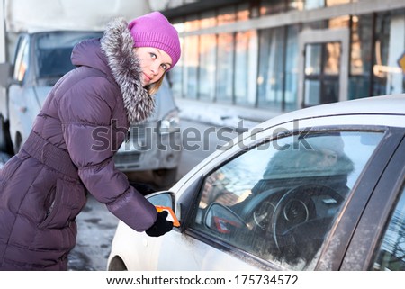 Woman in winter clothes cleaning car windows and mirrors before the trip