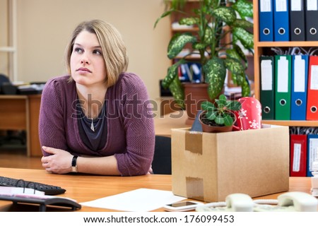 Thoughtful woman sitting in the office with the collected personal things in a box