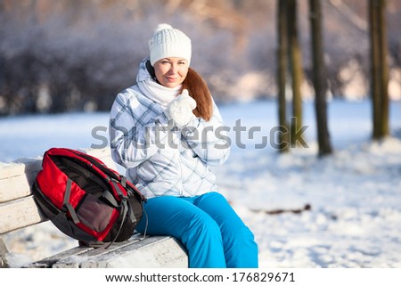 Young woman with backpack heating hands in mittens at winter, copyspace
