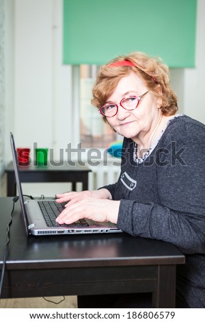 Elder woman looking at camera and typing on laptop keyboard