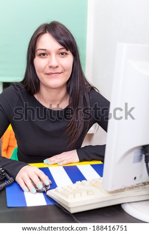 Smiling working woman behind computer monitor and keyboard