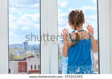 Little child looking through the window glass, copyspace, rear view