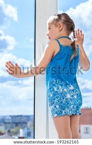 Small child looking through window, standing on windowsill