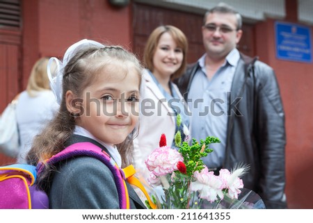 Young girl with flower and school bag looking at camera with her parents