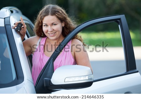 Smiling woman with car key in hand standing near vehicle opened door