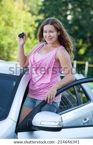 Smiling happy woman with new car and igniton key in hands