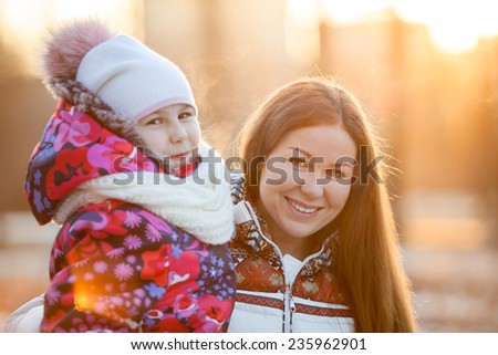 Portrait of Caucasian mother with a child at winter, a frosty evening, sunshine, sunset