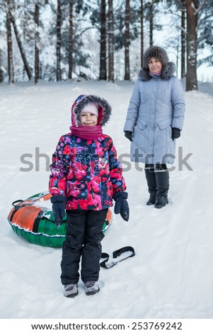 Smiling happy child with mature mother while tubing in winter forest