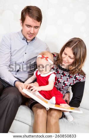 Baby girl turning pages of book while parents reading