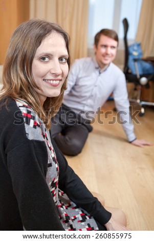 Young woman sitting floor in domestic room with man on background