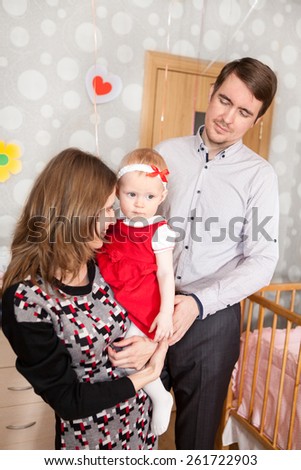 Mother holding her daughter in bed room with father standing near