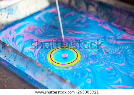 Close up view of making circle on water surface with stick and color inks