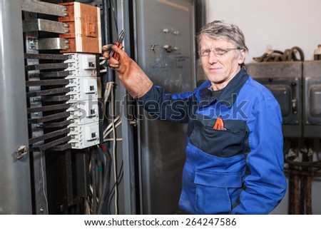 Electrician repairman in blue uniform holding pliers in rubber glove hand