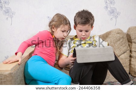 Preschool children having fun with pad while sitting on sofa in domestic room