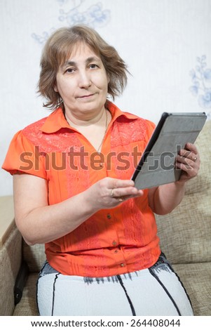 Smiling mature woman with pad in hands is in domestic room