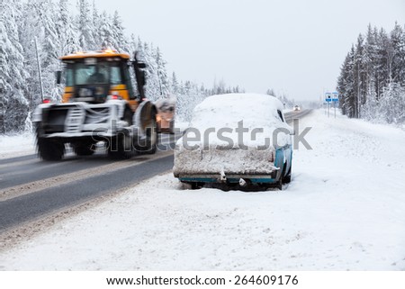 Tractor driving broken and abandoned on roadside car in snow and ice. Winter highway in north of Russia