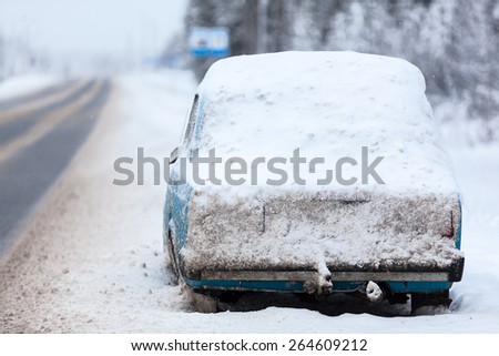 Broken abandoned car covered with snow and ice is on roadside at winter highway in north of Russia
