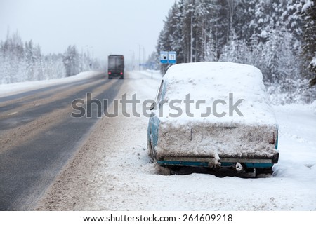 Cargo trucks driving along broken and abandoned on roadside car in snow and ice. Winter highway in north of Russia