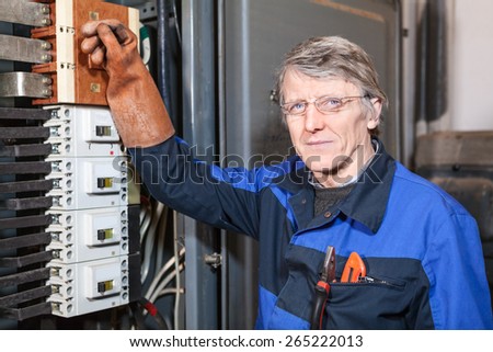 Mature electrician worker in rubber glove standing near high voltage industrial box