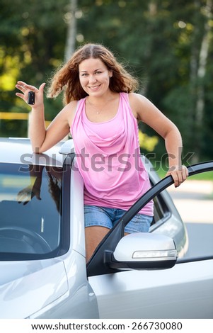 Joyful smiling girl with car keys in hand standing on footboard of vehicle