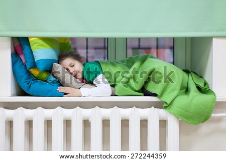 Young Caucasian child sleeping on the windowsill over heating radiator