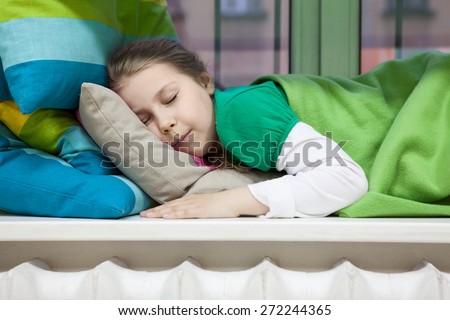 Close up of Caucasian girl sleeping on window sill with bright color pillows and blanket