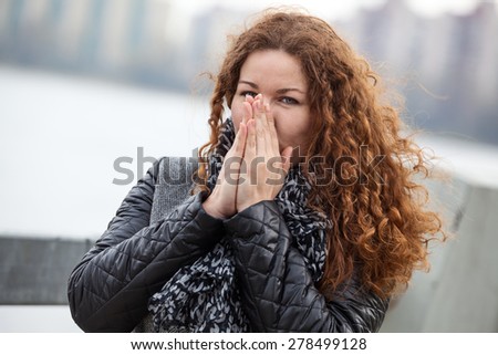 Frozen attractive woman with long curly hair blowing her hands while standing in cold weather