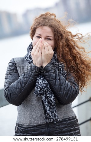 Beautiful woman in grey coat warming her hands while standing on cold wind