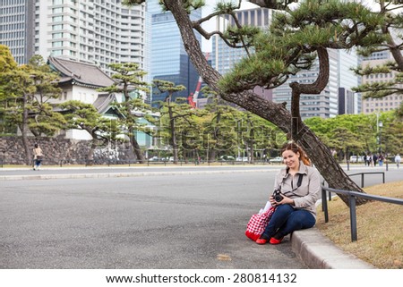 European woman a tourist with camera sitting in garden of Tokyo Imperial Palace, Japan. Copy space