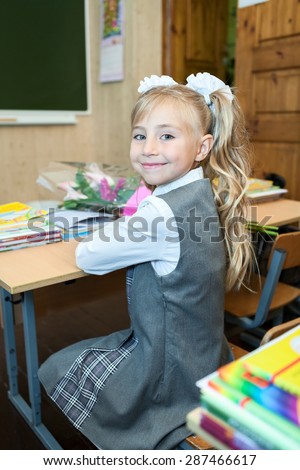 Happy schoolgirl in school uniform turning back while sitting at classroom