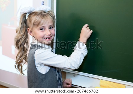 First grade pupil a girl writing on green blackboard at school lesson