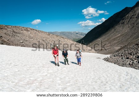 Three people family climbing mountain pass together in the snow at summer