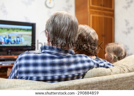Caucasian family from three people sitting on the couch and watching tv, rear view