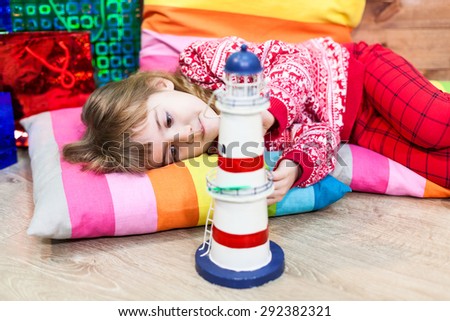 Young girl laying on color pillows at floor and holding toy, Christmas eve